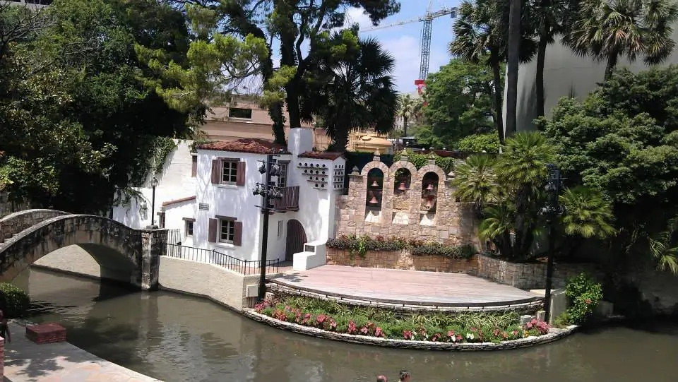 historic white washed house with wall of bells sitting on the bench of canal with historic stone bridge crossing the canal on left