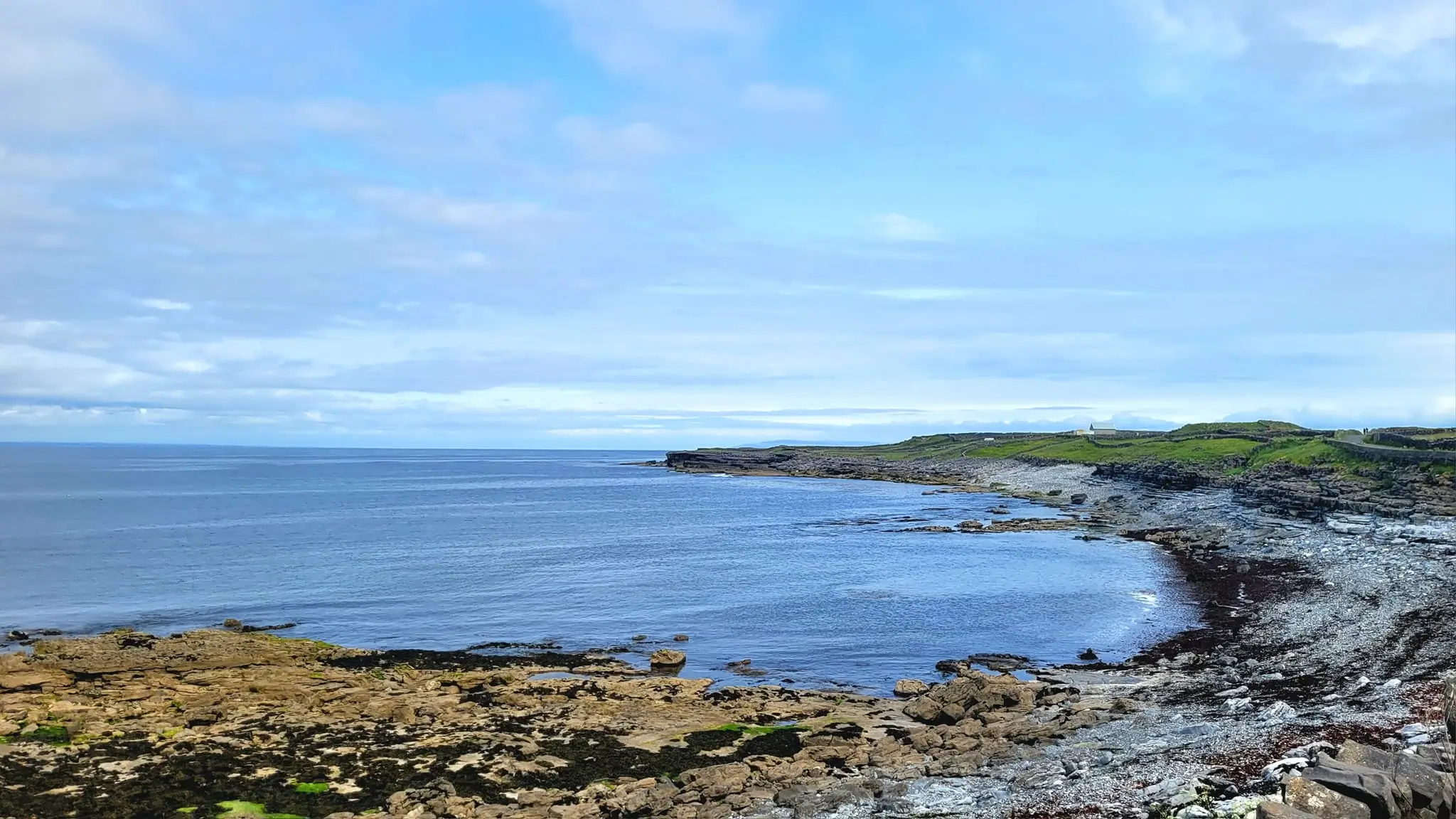 rocky black beach with green cliff and skyblue sea lagoon of Inis Mor