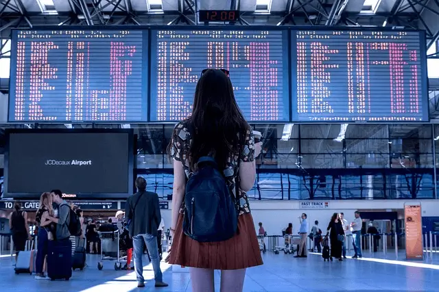 picture of girl with rucksack looking on flight departures board on airport