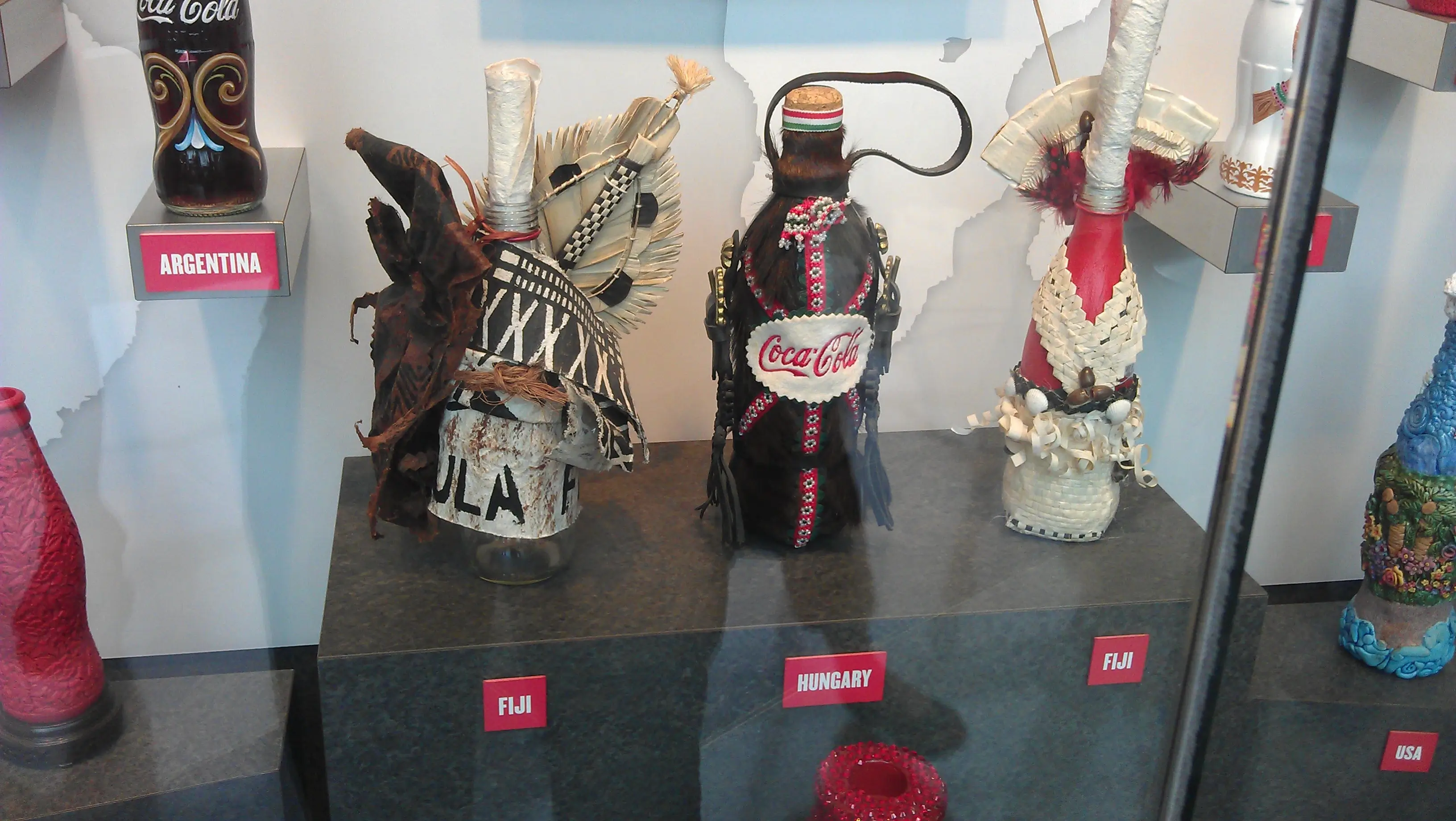 three colorful bottles of Coca-Cola decorated in style of traditional dresses of countries Fiji and Hungary