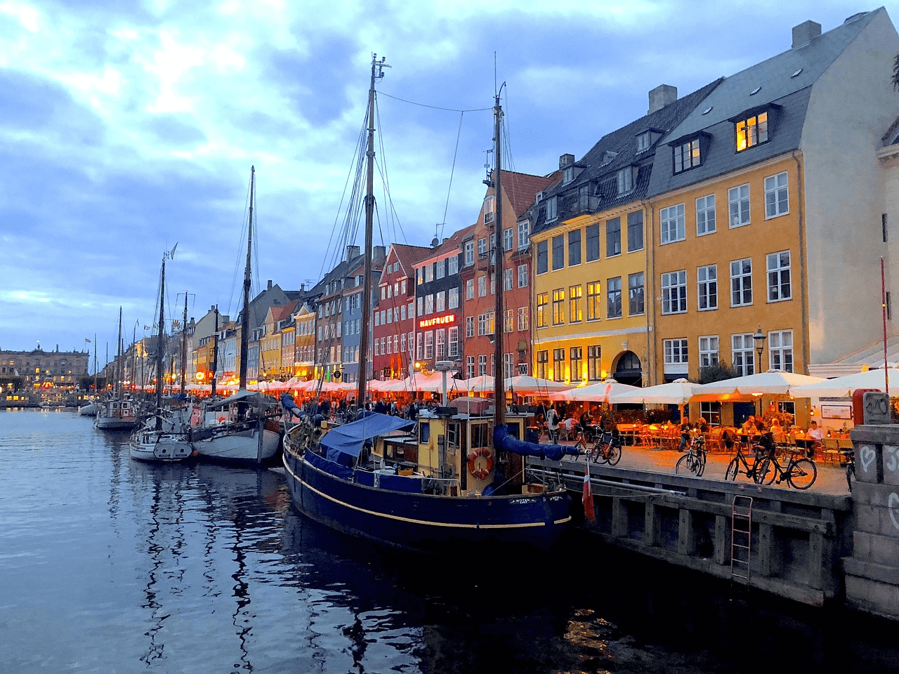 evening scenery of lit street with row of houses and boats on right and canal on left