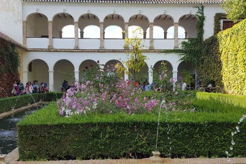 Generalife moorish style palace with artistically trimmed shrub in shape of cube surrounded by fountain streams and forming a frame to the cube shaped shrub