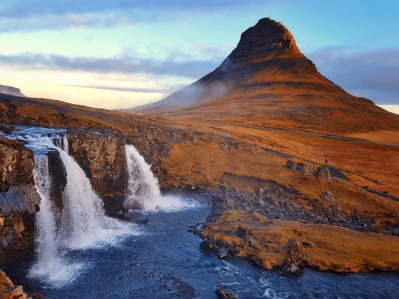 3 small waterfalls falling into water in front of red rock mountain