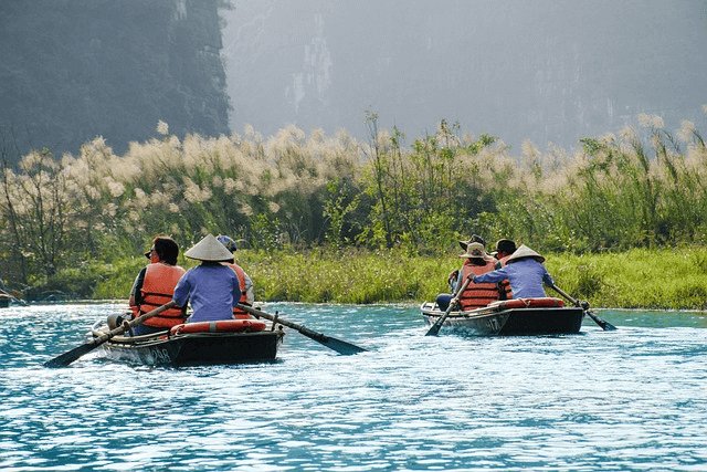 tourists on two small boats manoovered by locals in rice hat with hazy mountains in the background