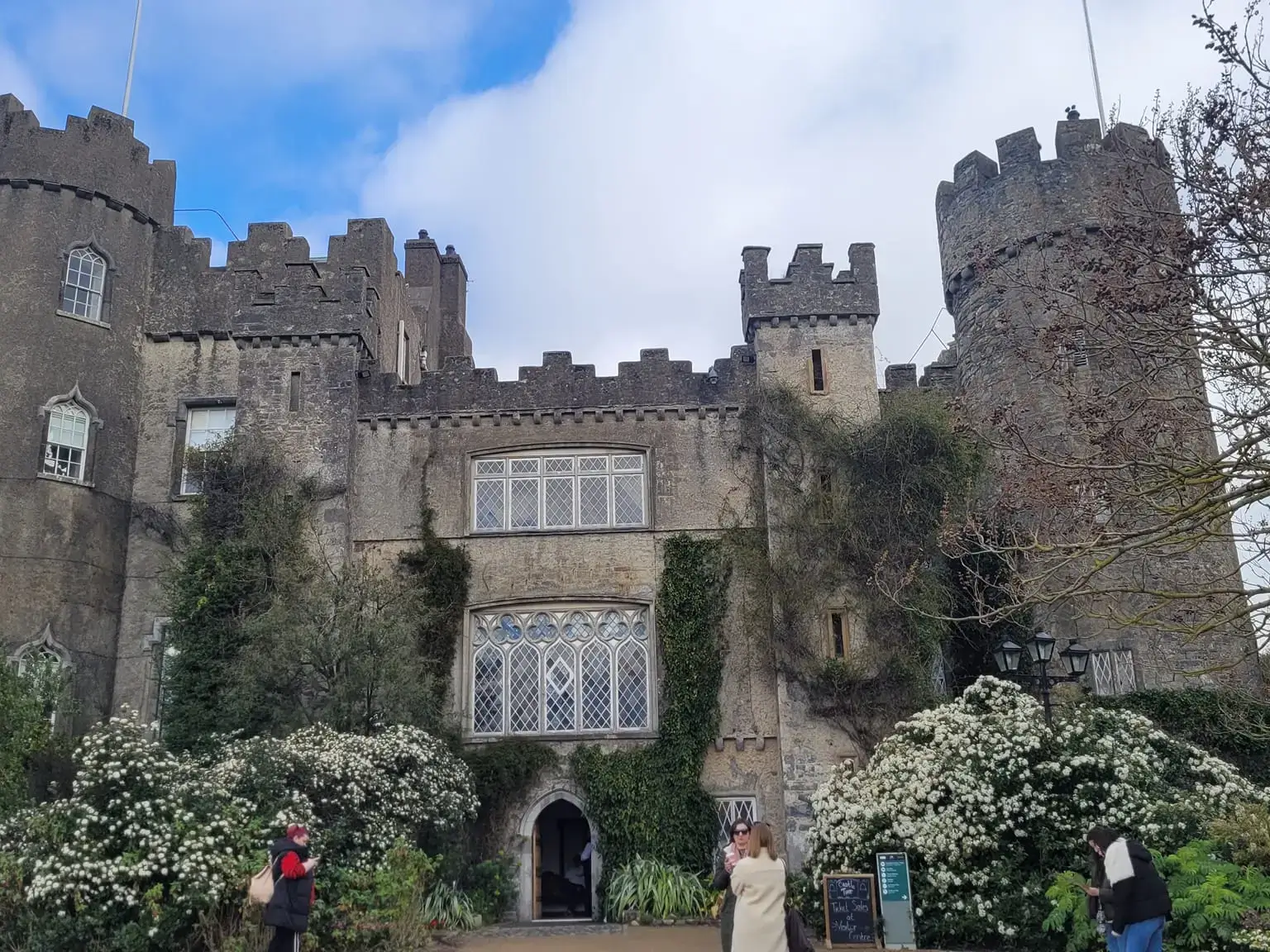 front entrance of Malahide castle surrounded but blooming trees antique petroleum lamps and few visitors in front of the entrance