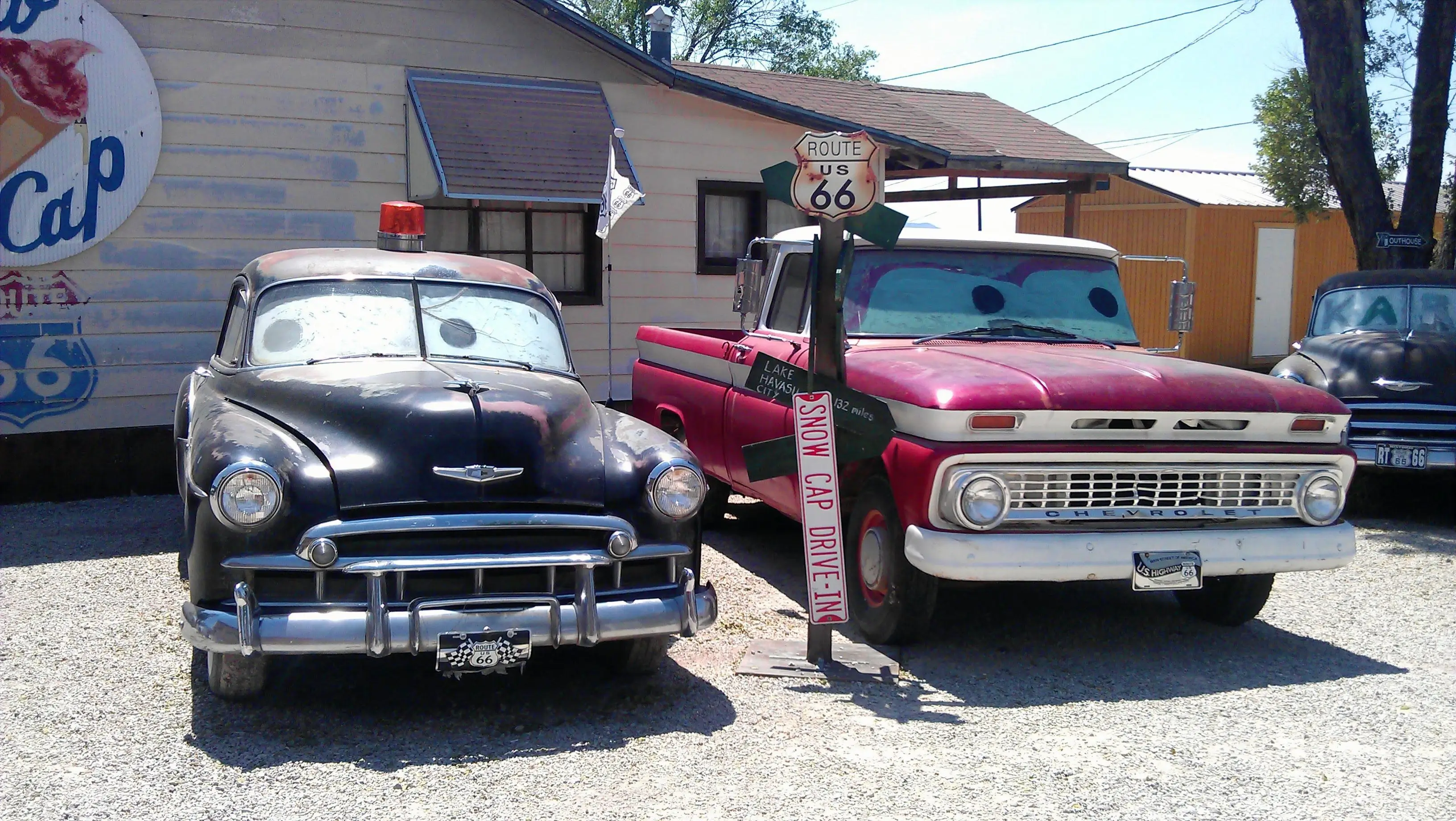 three historic cars in front of old wooden white house and pol with old sign route 66, on right black historic car and another black on left, in the middle old red truck.