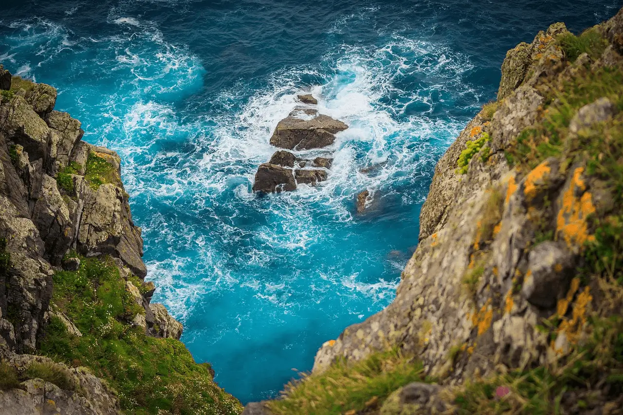 from first person view down from cliff on waves crashing over little rock sticking up from the turquase sea